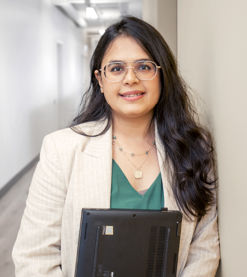 A female corporate employee wearing glasses and holding a laptop standing in the hallway of the LCBO Headquarters.